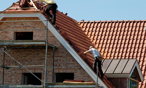 two men on top of a house roof fixing slates